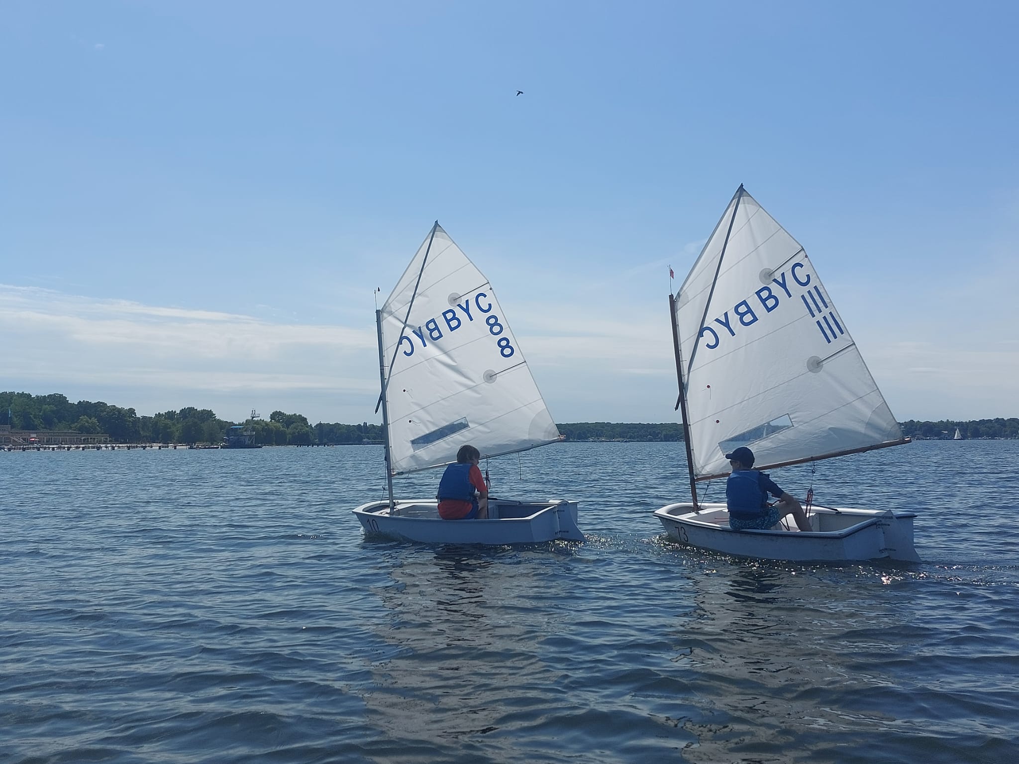 Zwei Optimisten-Segelboote mit Schülern nebeneinander auf dem Wannsee bei Sonnenschein