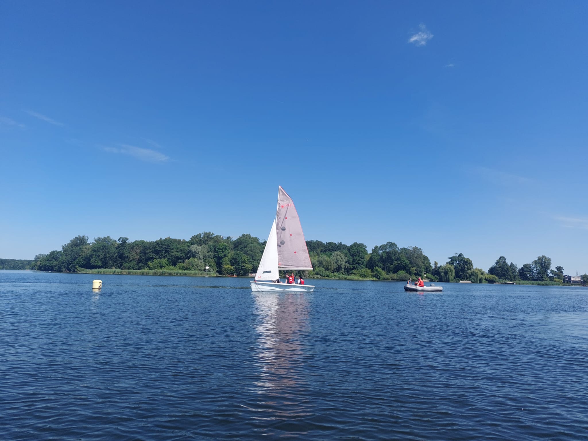 Segelboot mit mehreren Schülern und Begleitboot bei strahlendem Sonnenschein auf dem Wannsee